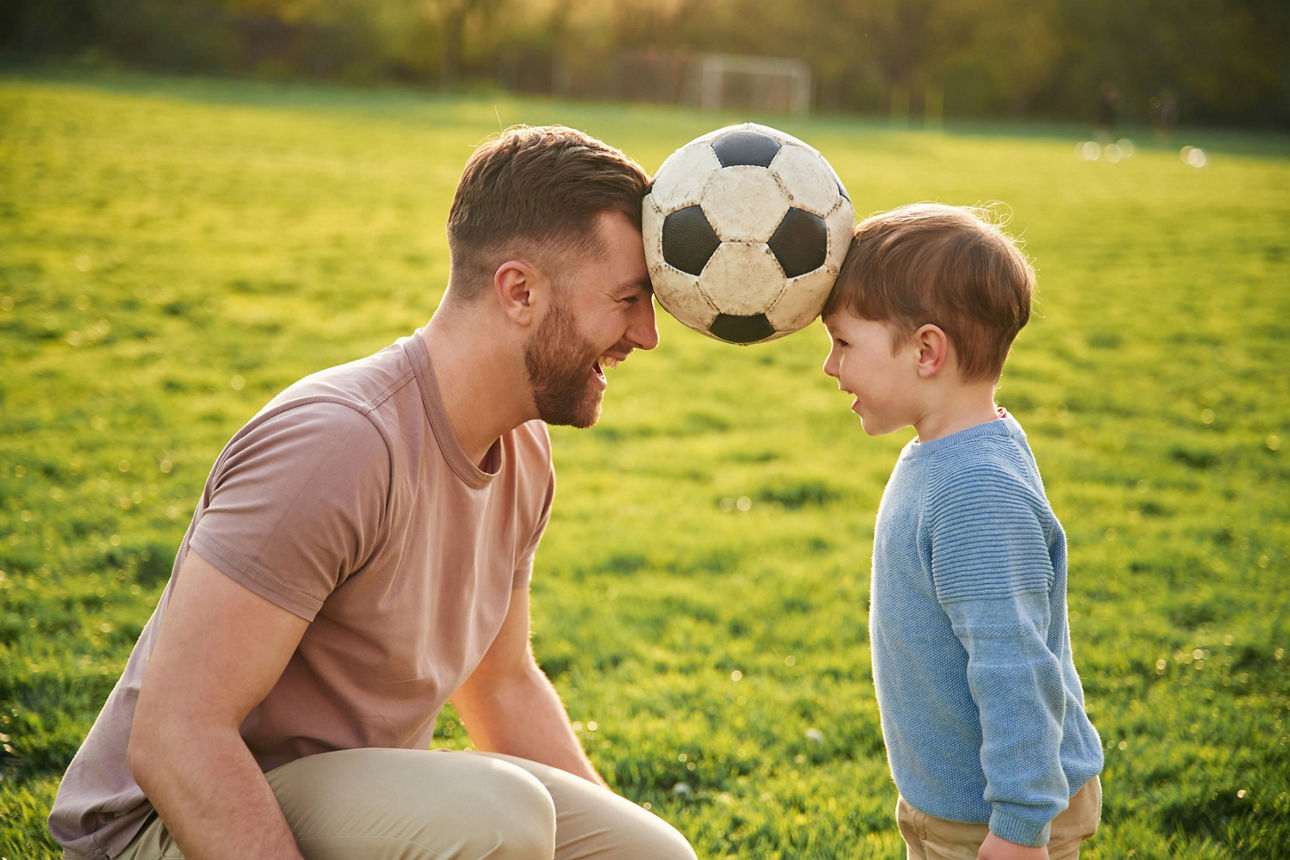 Vater und Sohn halten Fußball zwischen ihren Köpfen eingeklemmt