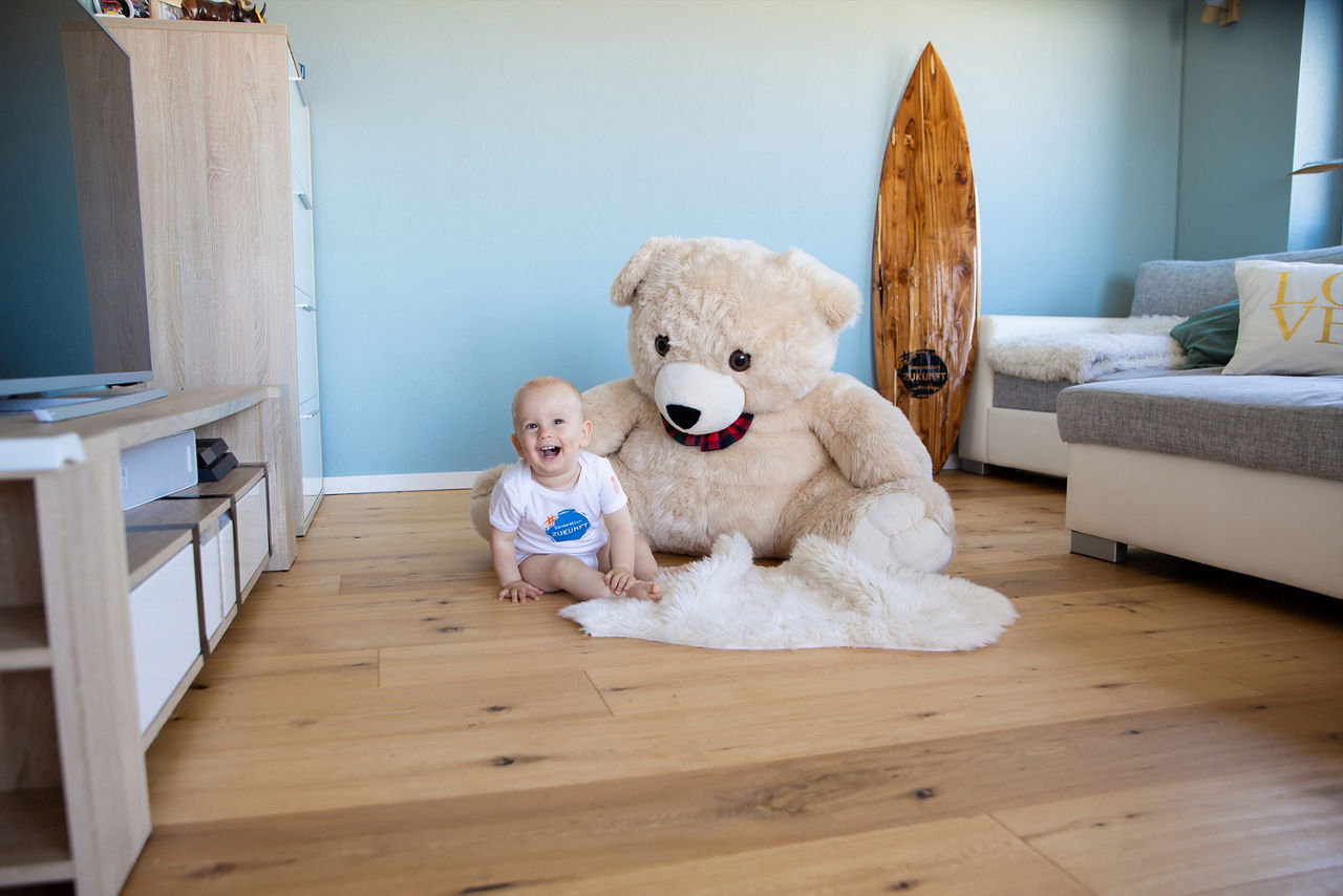 Baby sitzt vor einem großen Teddy-Bär im Wohnzimmer