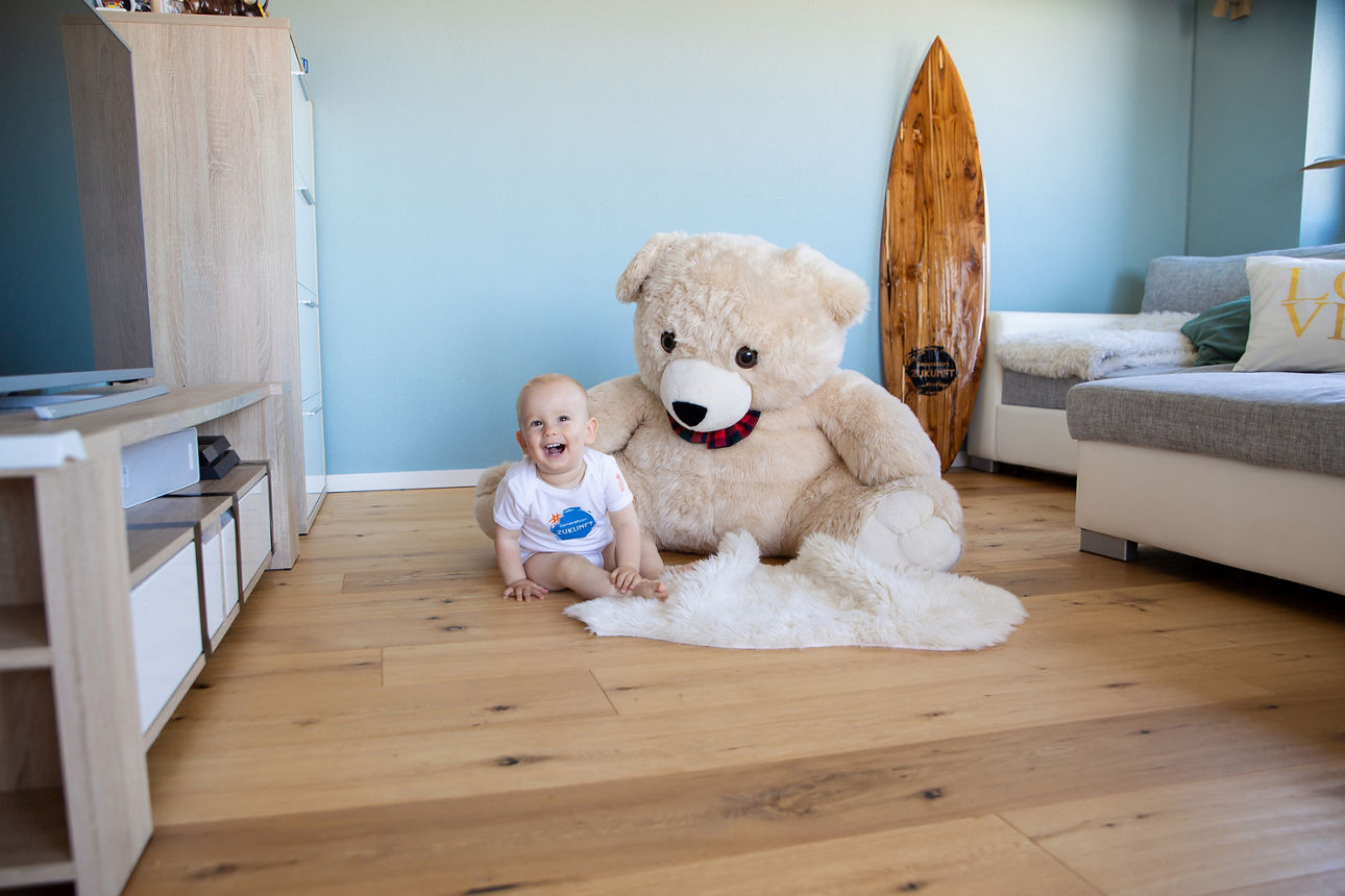 Baby sitzt vor einem großen Teddy-Bär im Wohnzimmer
