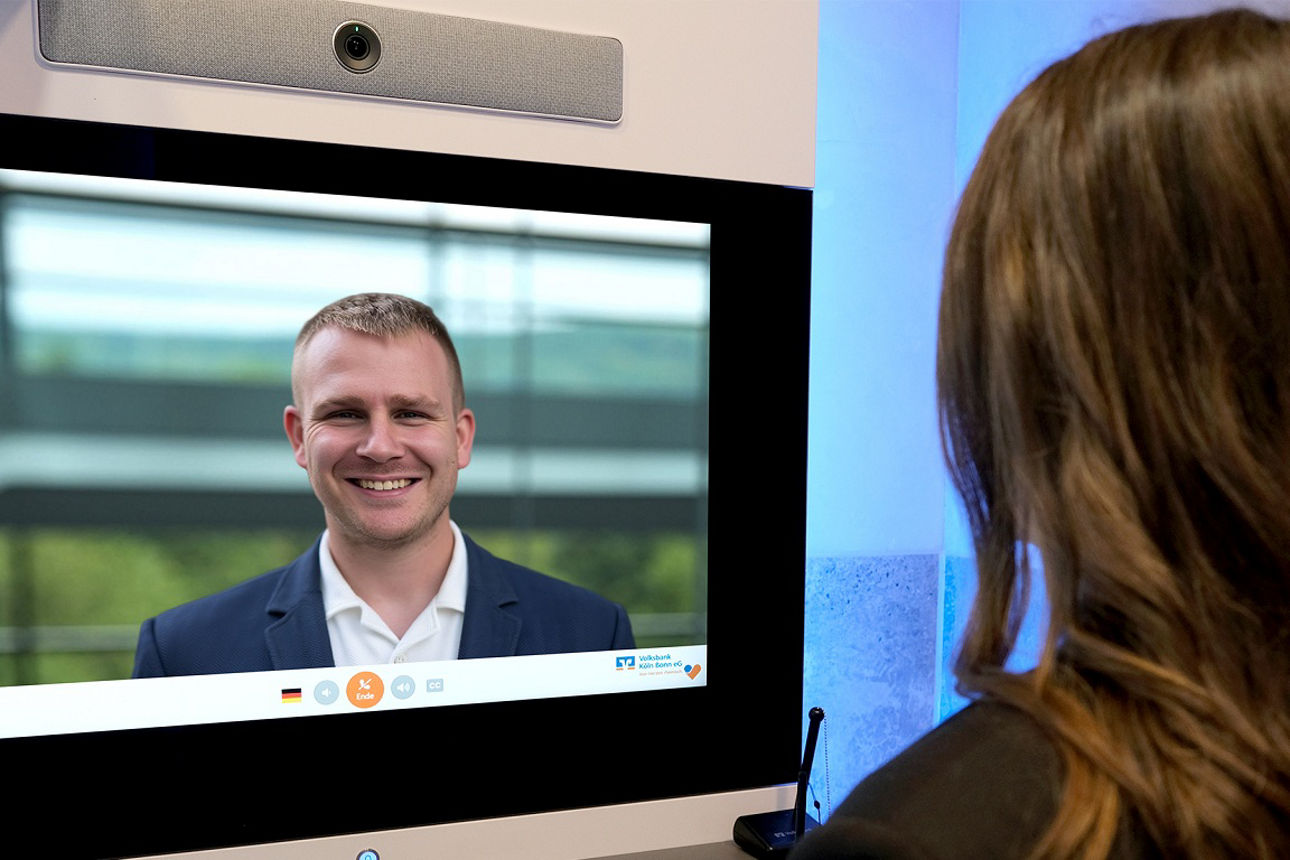 Eine Frau steht vor unserer EVI (virtueller Empfang) und lässt sich von einem Kundenberater beraten