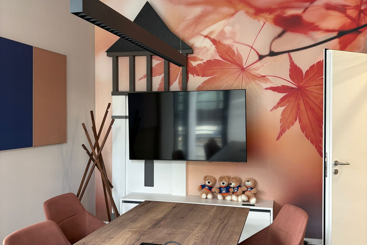 Neues Beratungszimmer mit braunem Holztisch und rot, braunen Stühlen, sowie einer Fototapete mit roten Blättern