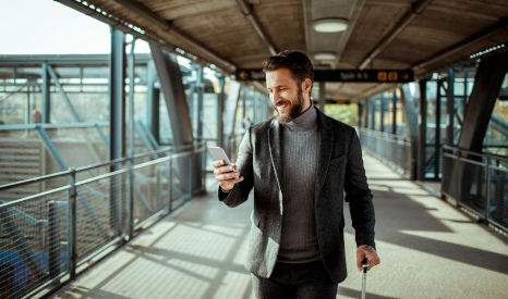 Mann auf einem Bahnhof mit Handy und Koffer in der Hand