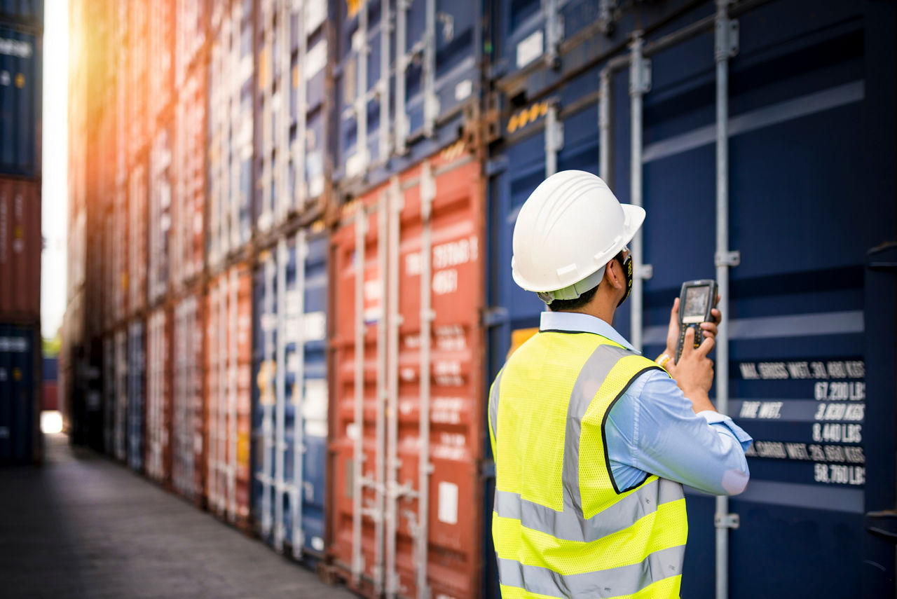 Mann in Arbeitskleidung steht mit einem Scanner vor Containern