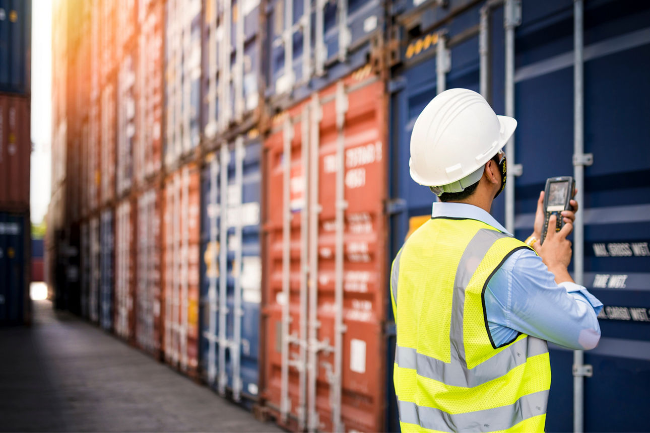 Mann in Arbeitskleidung steht mit einem Scanner vor Containern