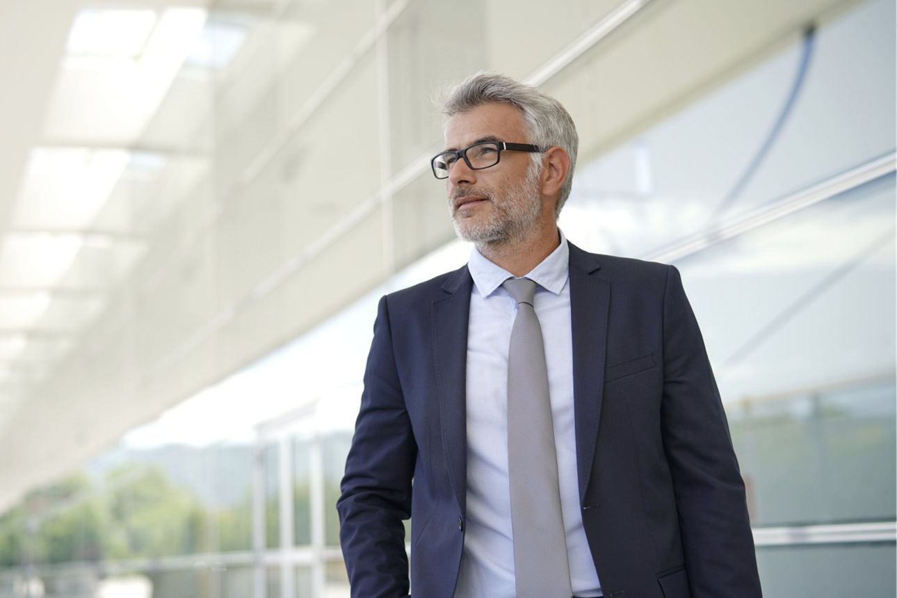 Mann im Anzug steht vor einem verglasten Gebäude