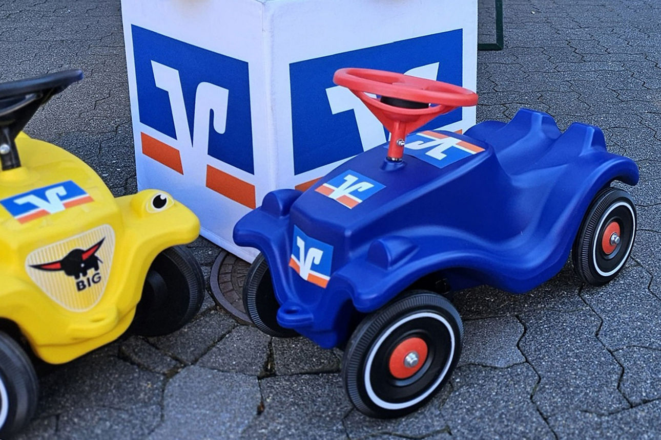 Zwei Volksbank Bobbycars stehen vor einem Volksbank Würfel