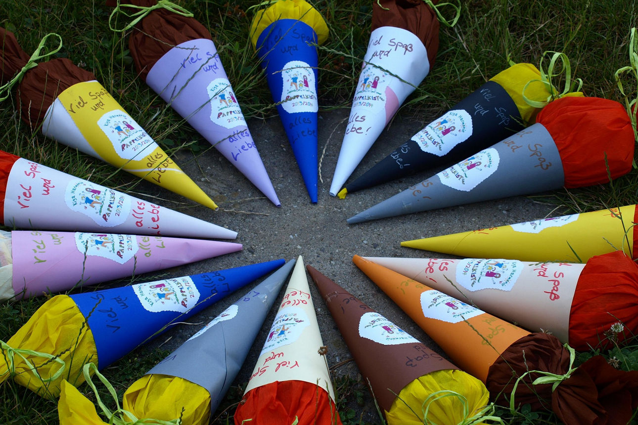 Fünfzehn verschiedenfarbige Schultüten liegen mit der Spitze nach innen auf dem Bogen im Kreis