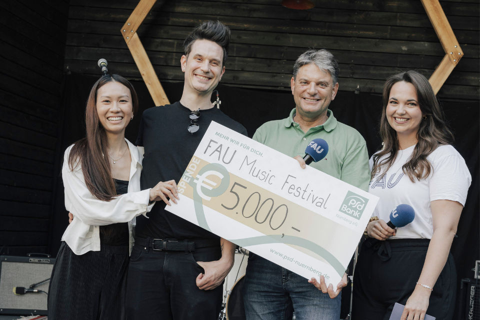 Zwei Kolleg:innen der PSD Bank Nürnberg überreichen der FAU einen den Spendencheck in Höhe von 5.000€.