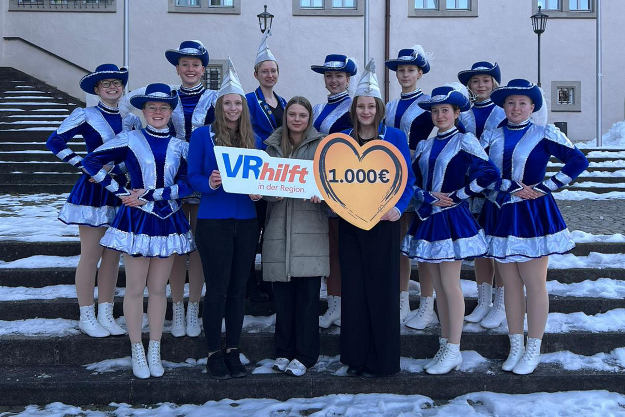 Auf dem Bild stehen auf einer schneebedeckten Treppe die Damen der Prinzengarde Faldungen sowie eine Mitarbeiterin der VR-Bank. Sie halten ein Schild in Herzform mit der Spendenaufschrift in der Hand. 