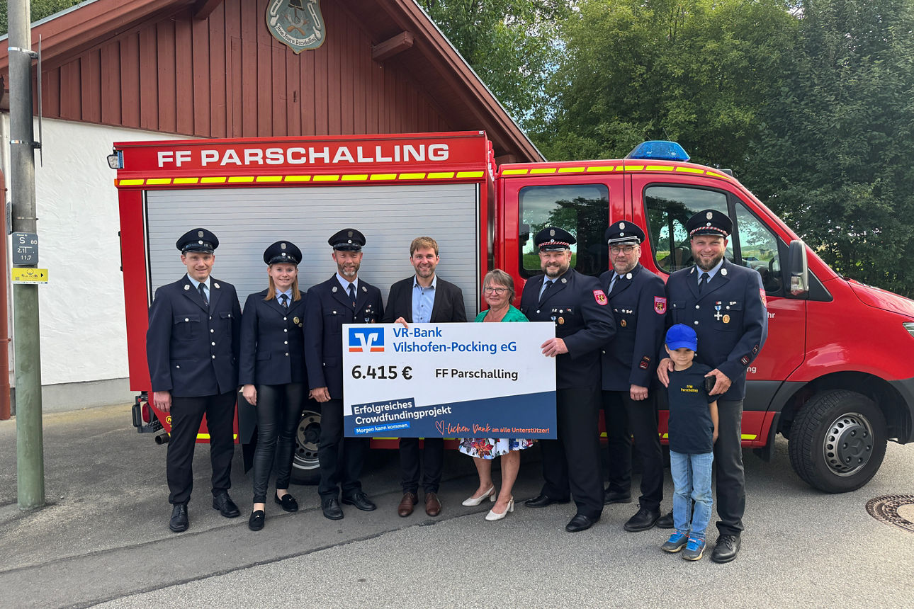 Mitglieder der Feuerwehr und Mitarbeiter der Bank mit Spendenscheck vor einem Feuerwehrauto
