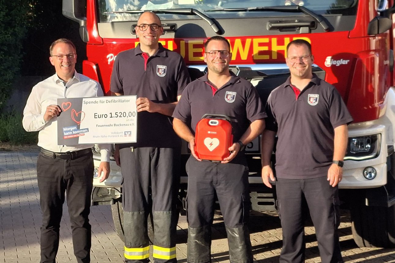 Vier Personen stehen vor einem Feuerwehrwagen