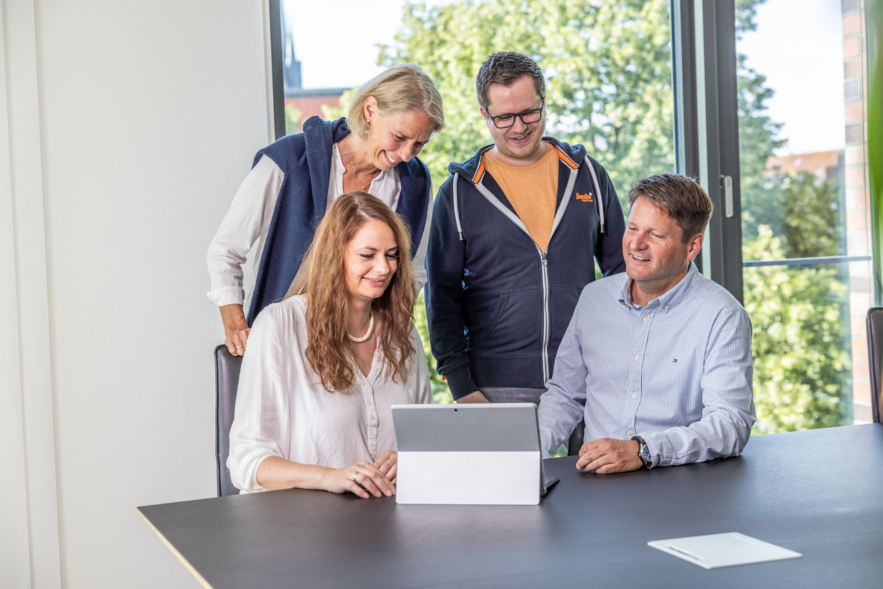 Vier Personen blicken auf einen Laptop, der auf einem Besprechungstisch steht.