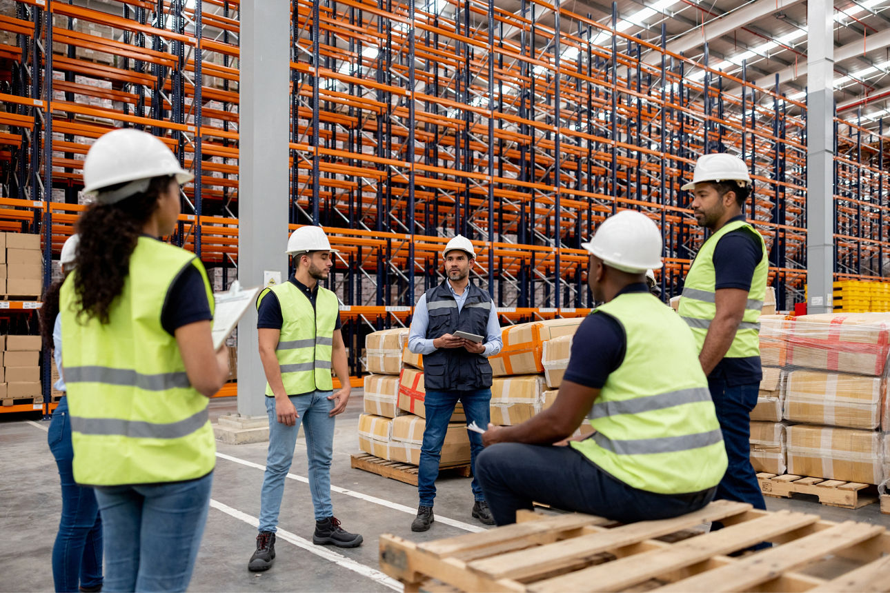 In einer Produktionshalle erklärt eine Produktionsleiterin zwei Besuchern den Produktionsablauf