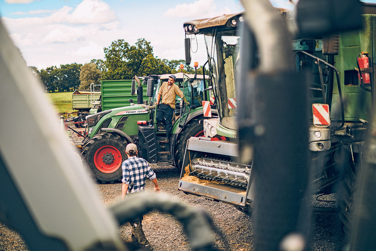 Zwei Landwirte stehen mit ihren Treckern und Maschinen auf einem Feld