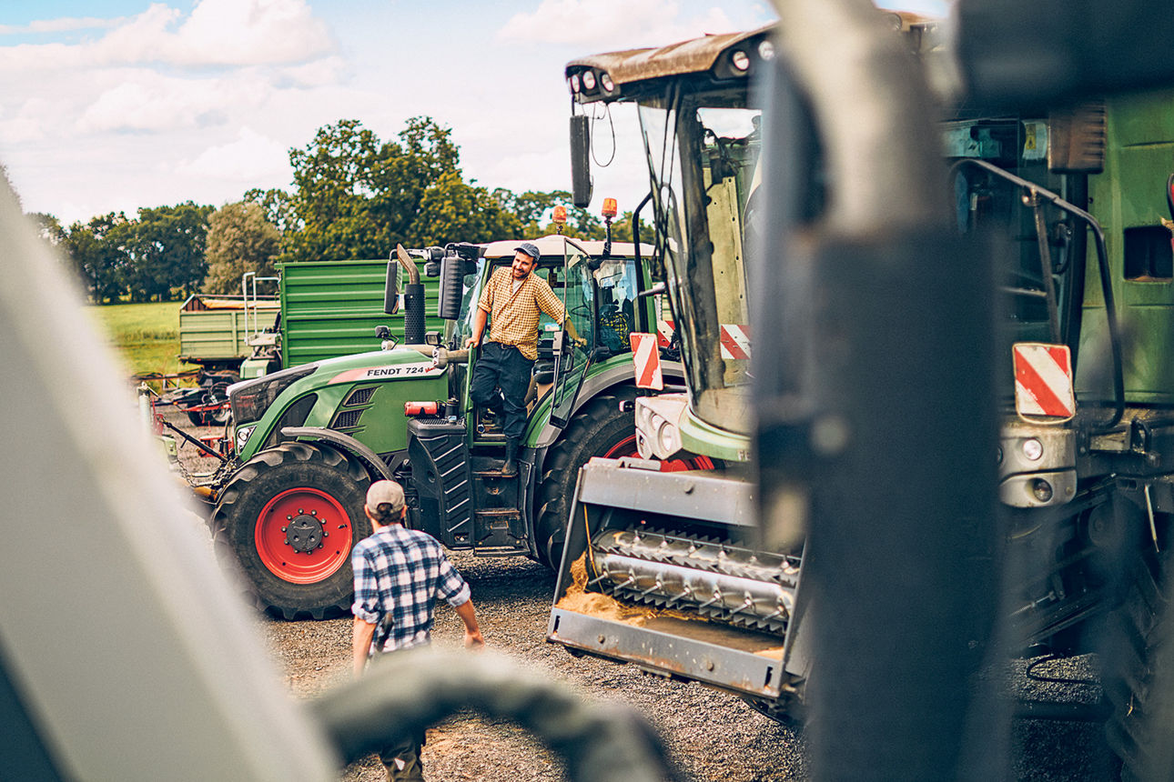 Zwei Landwirte stehen mit ihren Treckern und Maschinen auf einem Feld