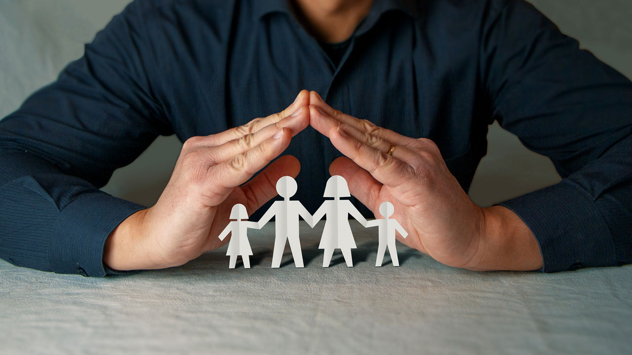Ein Mann hält schützend seine Hände über Figuren, die eine Familie symbolisieren.
