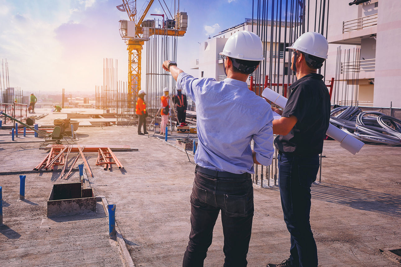 Zwei Männer mit Baustellenhelm unterhalten sich auf einer großen Baustelle.