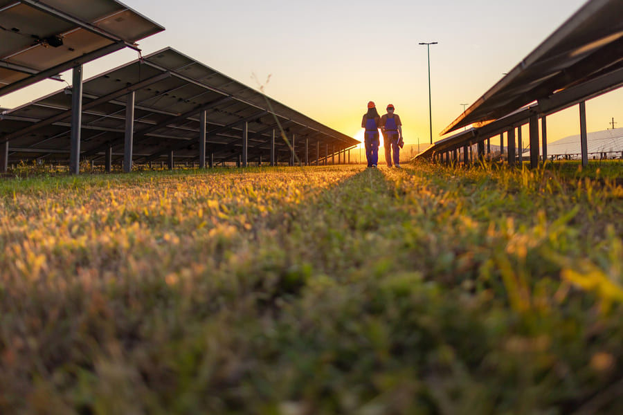 Zwei Arbeiter laufen bei Sonnenuntergang über ein Feld mit Solaranlagen