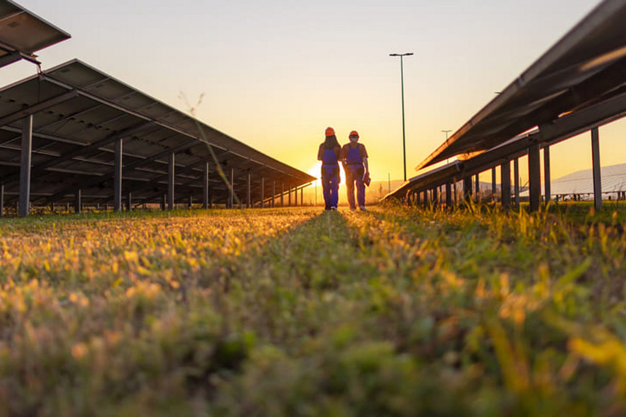 Zwei Arbeiter laufen bei Sonnenuntergang über ein Feld mit Solaranlagen