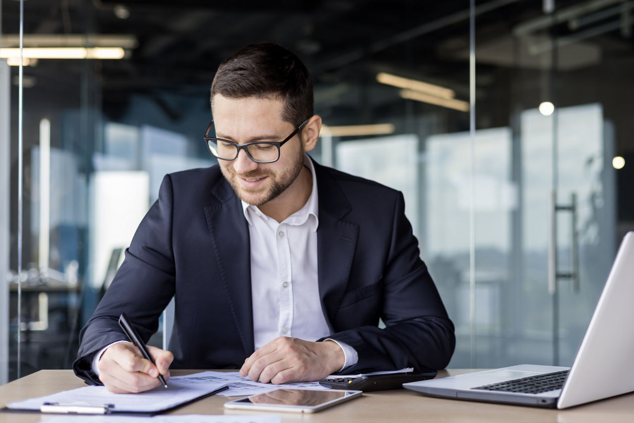Young businessman working in the office at the workplace with documents, signing an agreement, working with accounts
