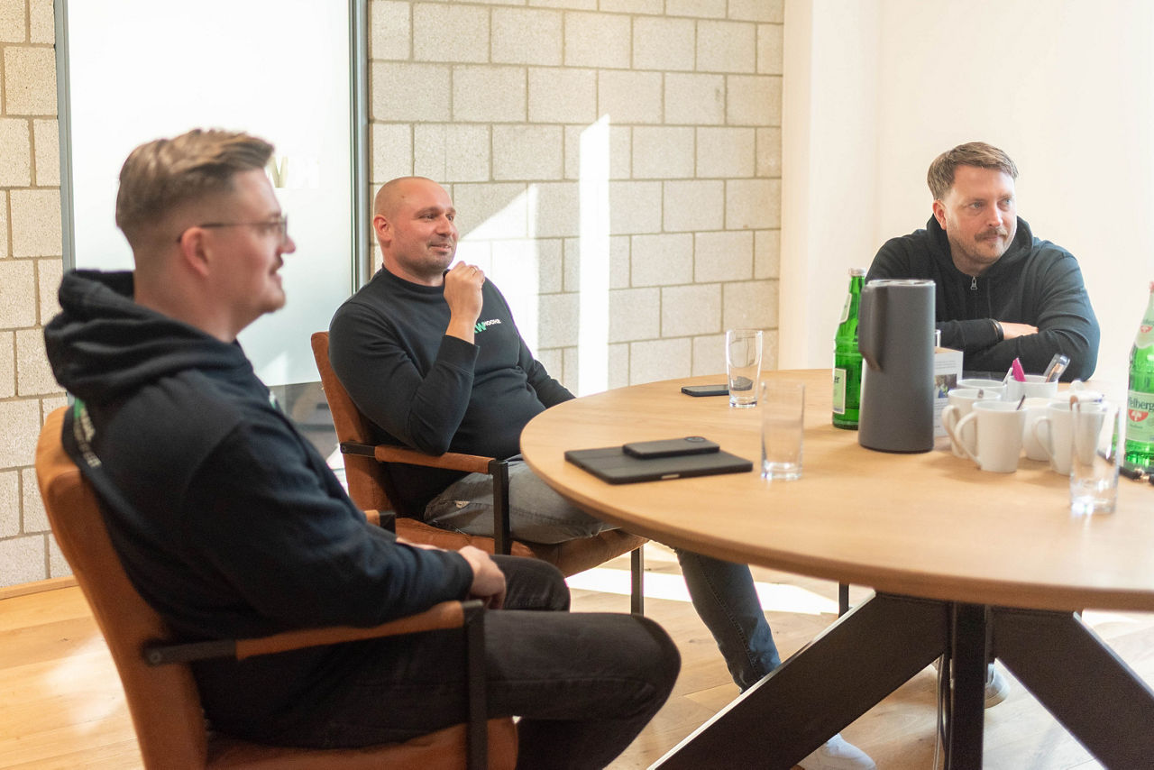 Drei Männer sitzen um einen Konferenztisch