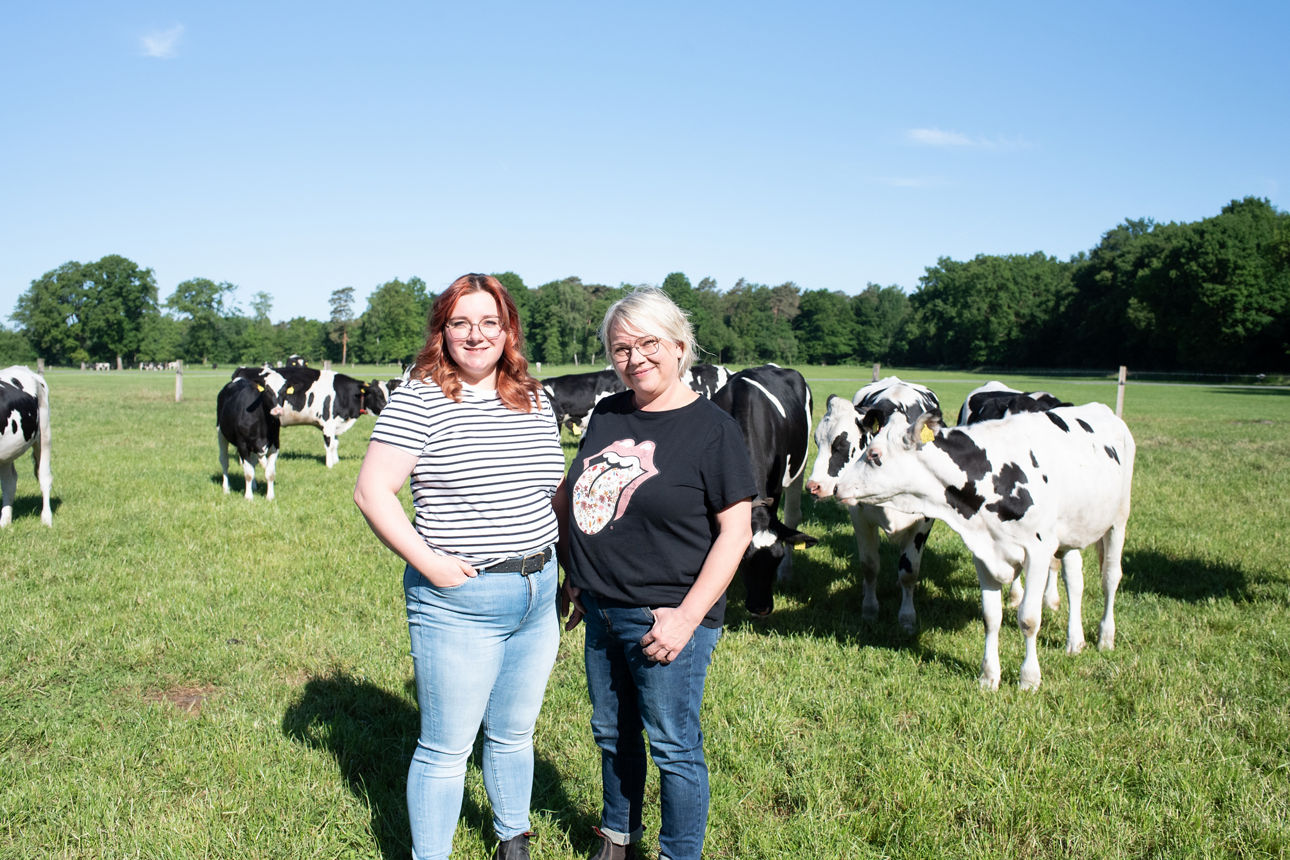 Agrarkundinnen stehen zu zweit lächelnd auf einer Kuhweide. 