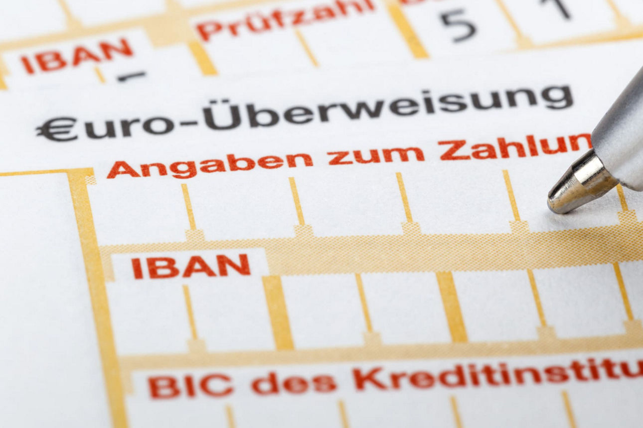 Nahaufnahme eines leeren Überweisungsbelegs, welcher gerade mit einem Kugelschreiber ausgefüllt wird.