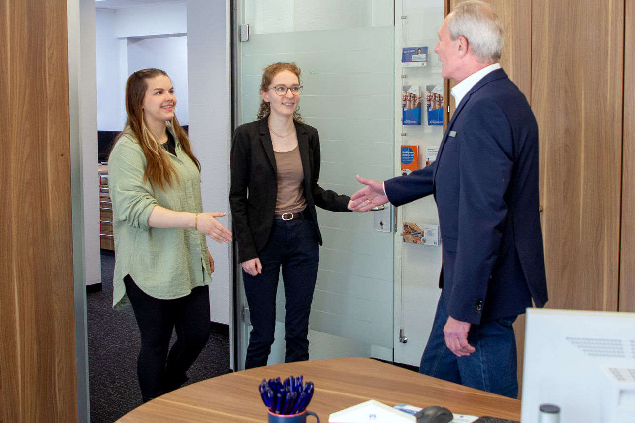 Ein Mitarbeiter im Büro begrüßt zwei Damen
