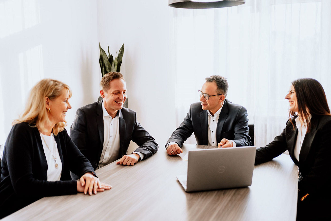 Vier Berater des Family Office sitzen am Tisch vor einem Laptop in einem Beratungszimmer.