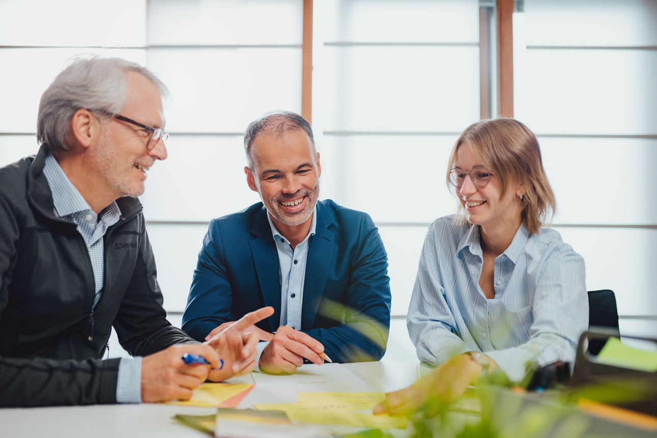 Drei Mitarbeitende sitzen am Tisch und unterhalten sich