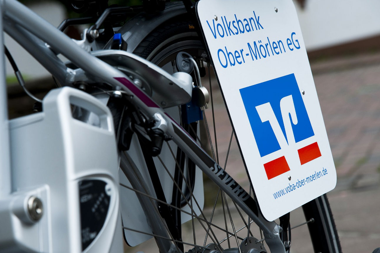 Ein Elektrofahrrad und eine Plakette mit dem Logo der Bank