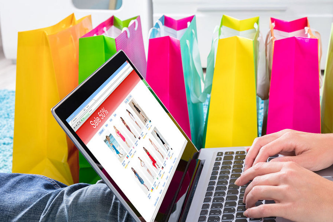 Laptop auf dem Sonderangebote angezeigt werden und im Hintergrund bunte Einkauftüten