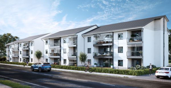 Mehrstöckige Wohnhäuser mit Balkonen und Satteldächern entlang einer Straße mit parkenden Autos und Gehwegen. 