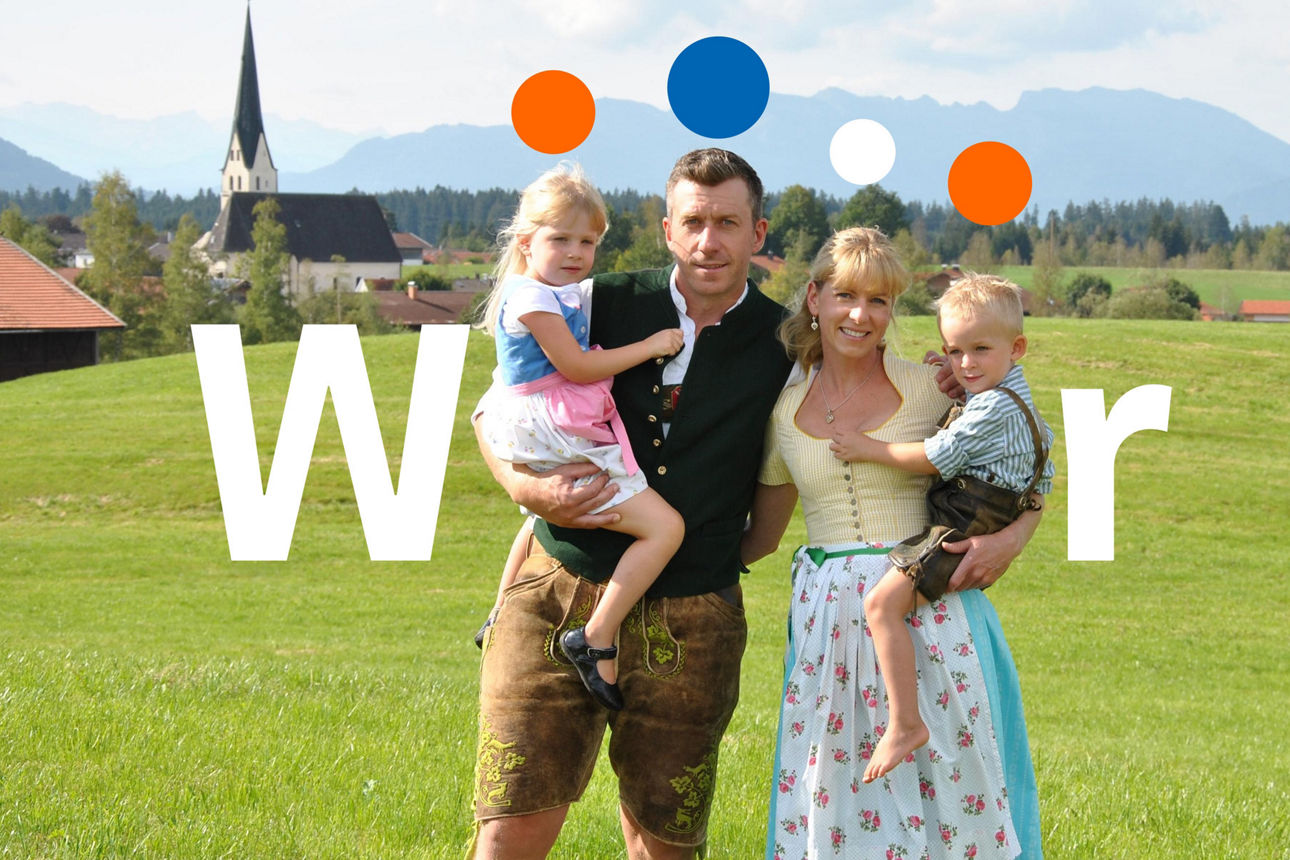 Eine Familie steht auf einer Wiese. Im Hintergrund Berge.