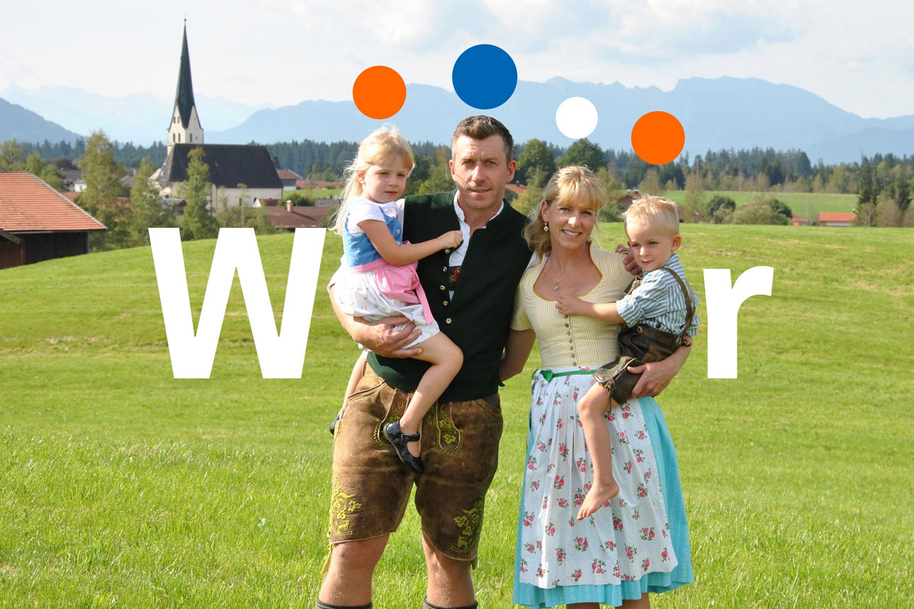 Eine Familie steht auf einer Wiese und hat Spaß. Im Hintergrund Berge