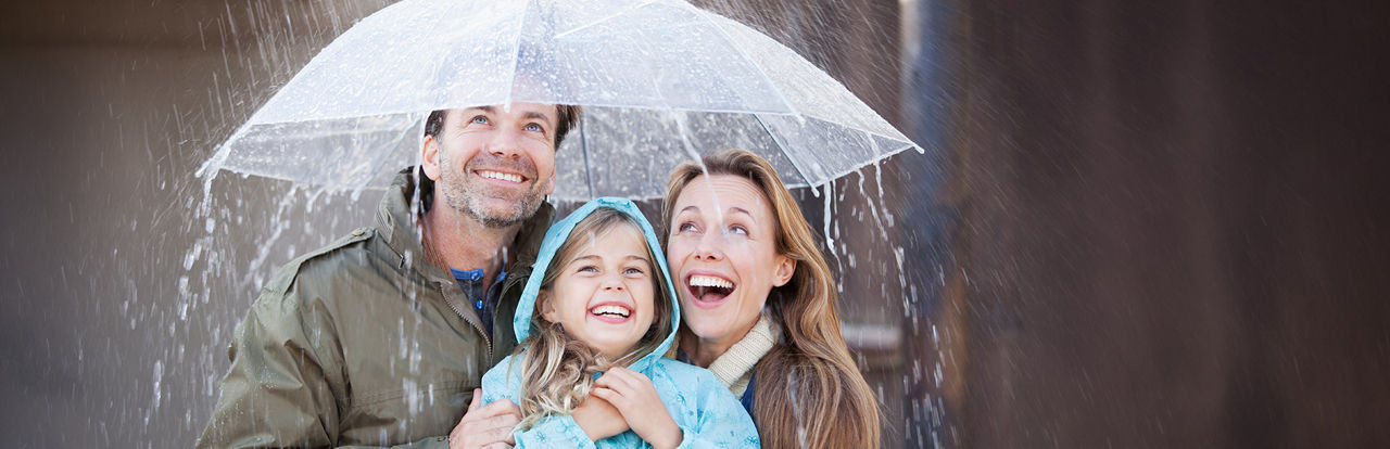 Familie steht lachend unter dem Regenschirm