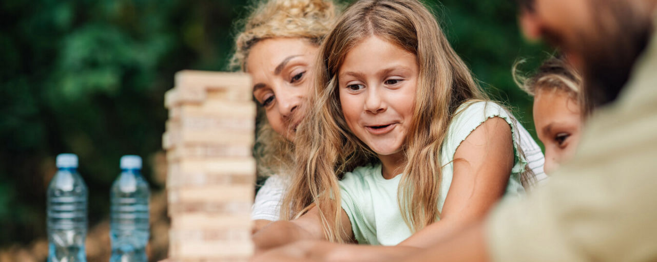 Mädchen setzt einen Stein auf einen Jenga-Turm.