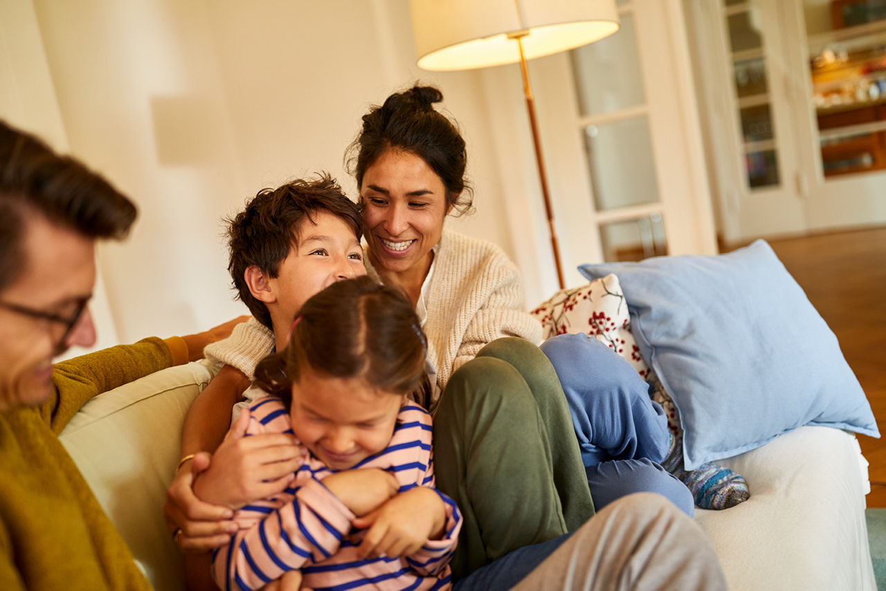 Eine Frau und ein Mann sitzen lachend mit zwei Kindern auf dem Sofa.