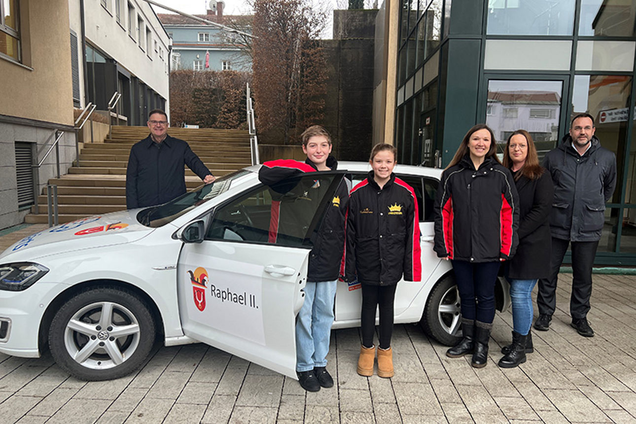 Kinderprinzenpaar steht mit den Vorständen Herr Schöpfel u. Herr Zeiler und zwei Damen vor einem Auto