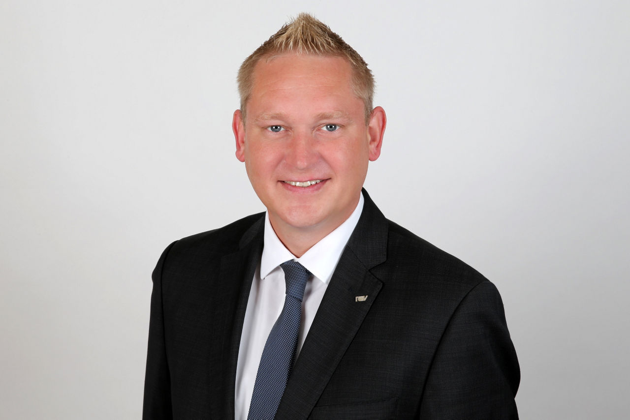 Ein lächelnder Mann in einem Anzug schaut in die Kamera.