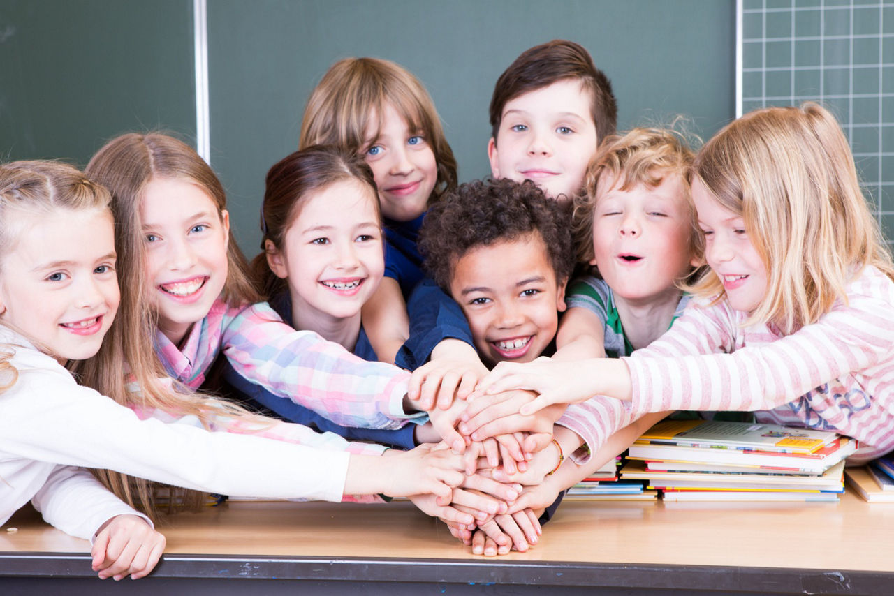Schüler vor einer Tafel legen ihre Hände aufeinander