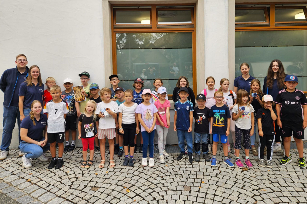 Eine Gruppe von 23 Kindern schaut mit fünf Mitarbeitenden des Jugendmarktes in die Kamera