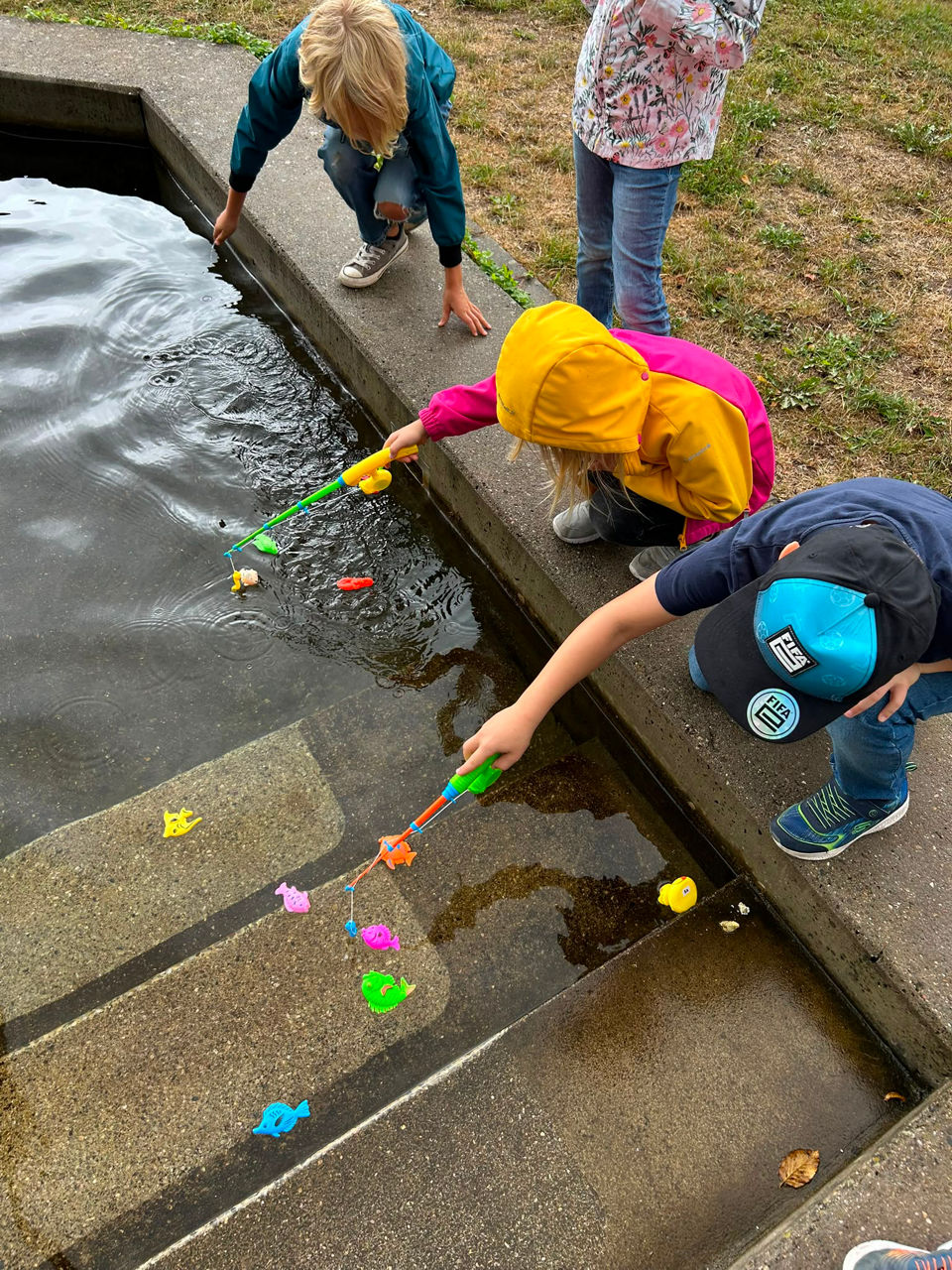 Zwei Kinder versuchen, aus einem Brunnen Plastikfische herauszuangeln