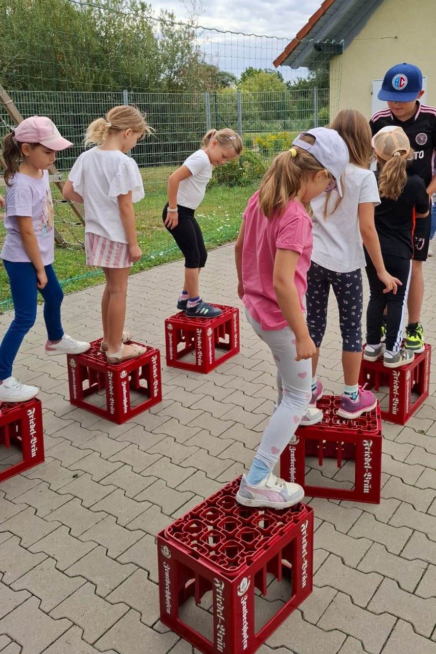 Kinder balancieren über umgedrehte Getränkekästen, die mit einem Meter Abstand aufgestellt sind