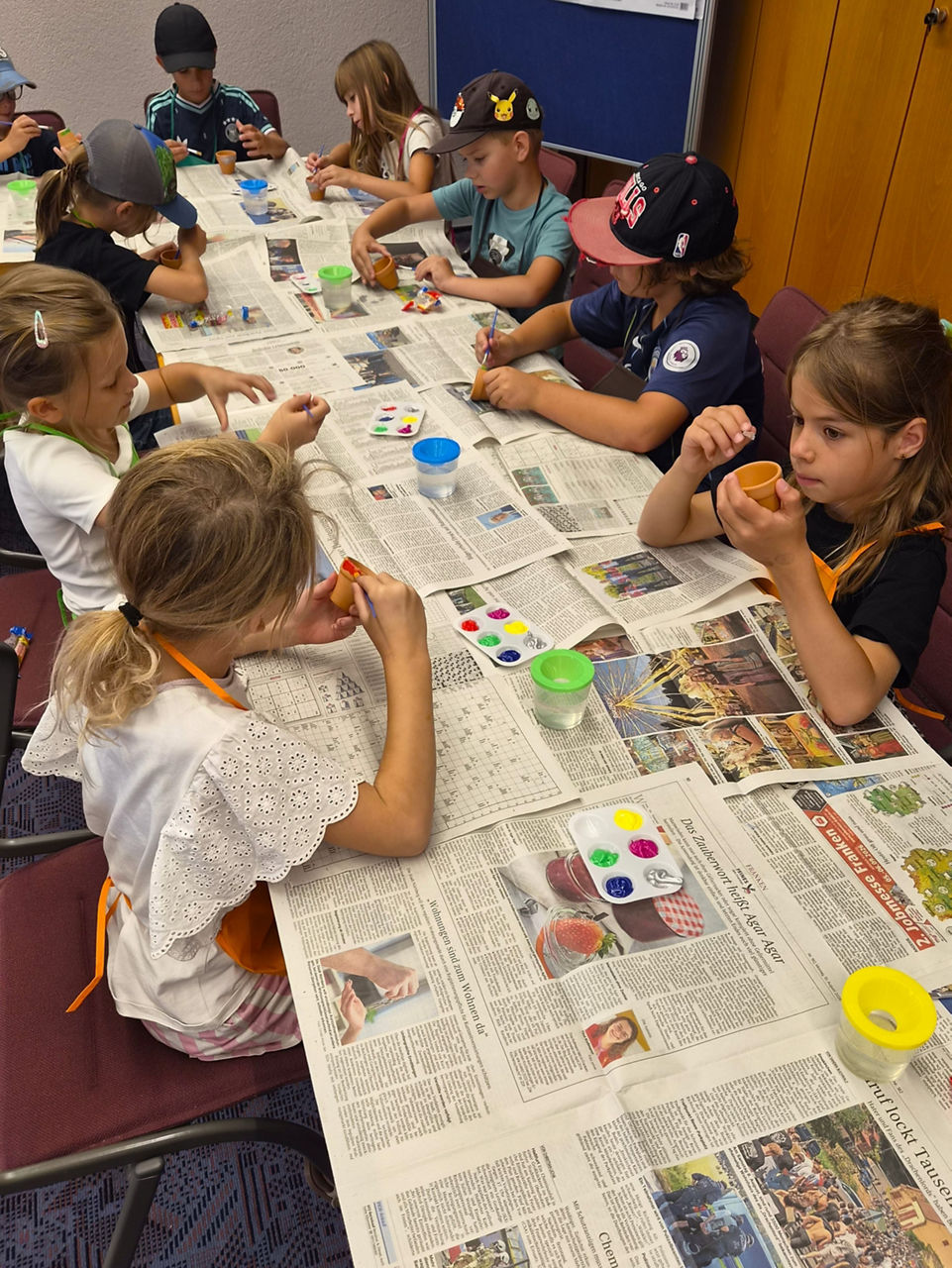 Acht Kinder sitzen an einem mit Zeitung abgedeckten Tisch und malen mit Fingerfarben