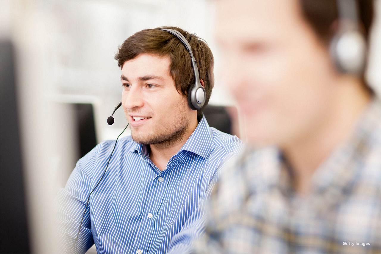 Ein Call-Center Mitarbeiter hat en Headset auf und lächelt.