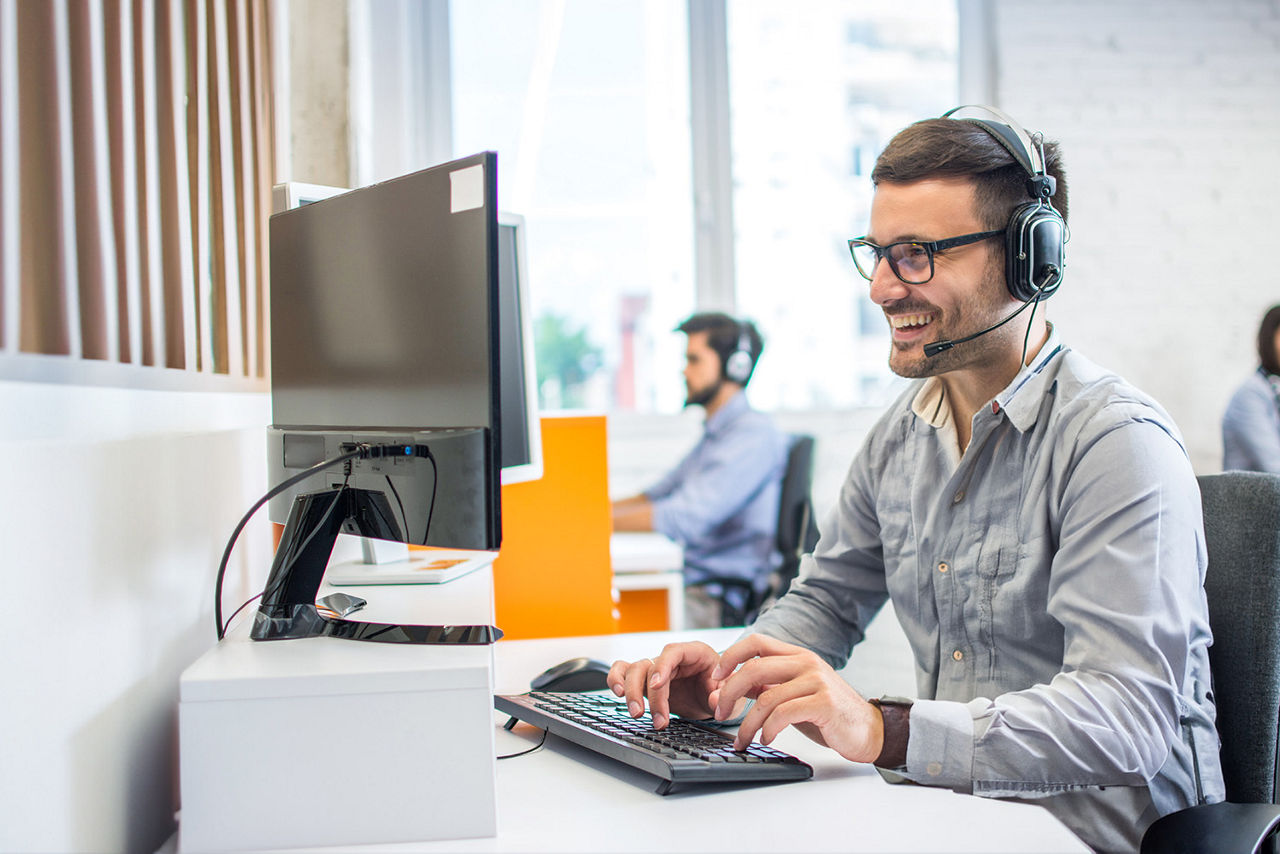 Mann sitzt vorm Computer im Büro und telefoniert mit Headset
