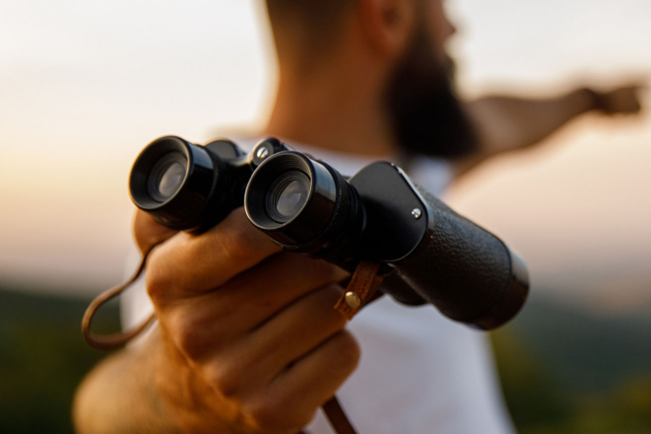 Mann mit Fernglas zeigt auf den Horizont