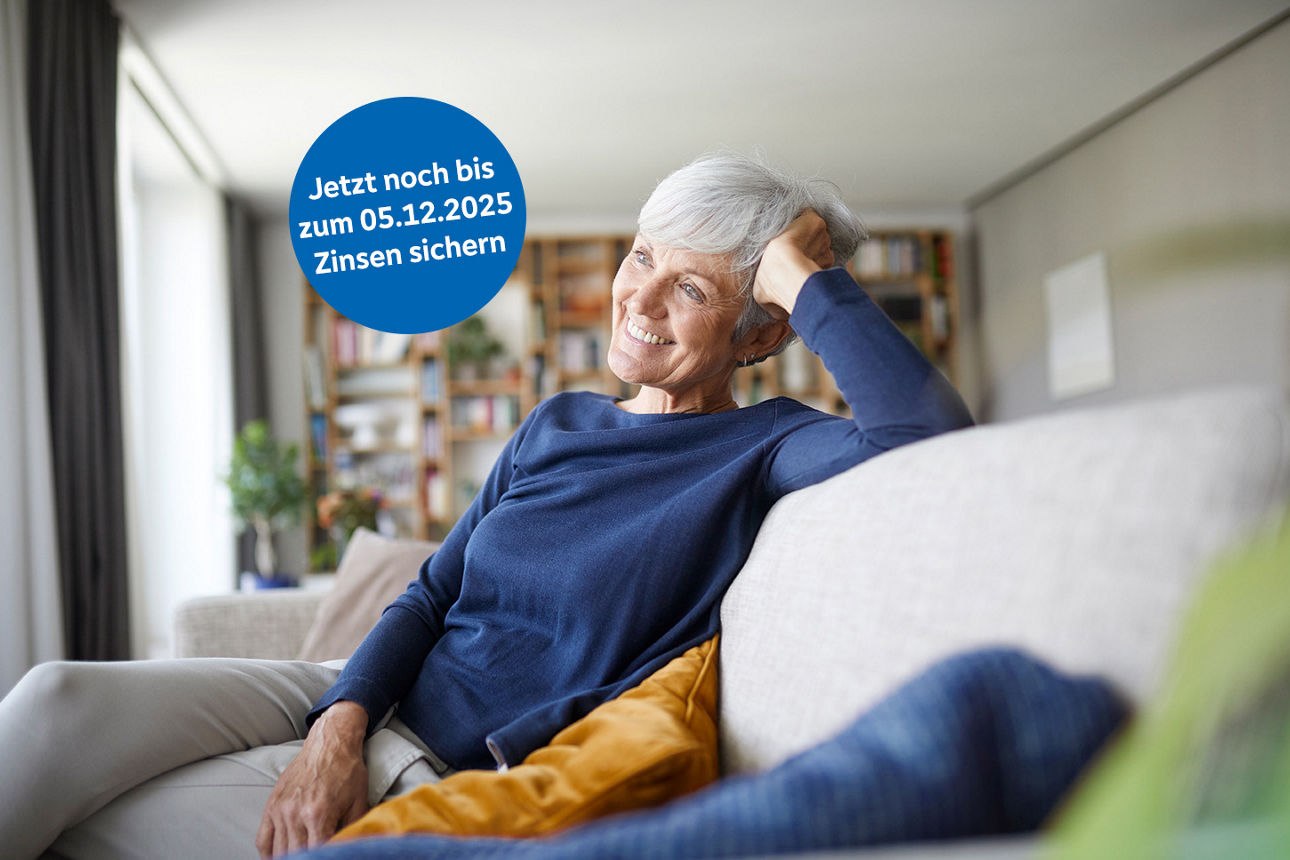 Eine Frau sitzt lächelnd mit überschlagenen Beinen auf dem Sofa und stützt ihren Kopf mit ihrer rechten Hand