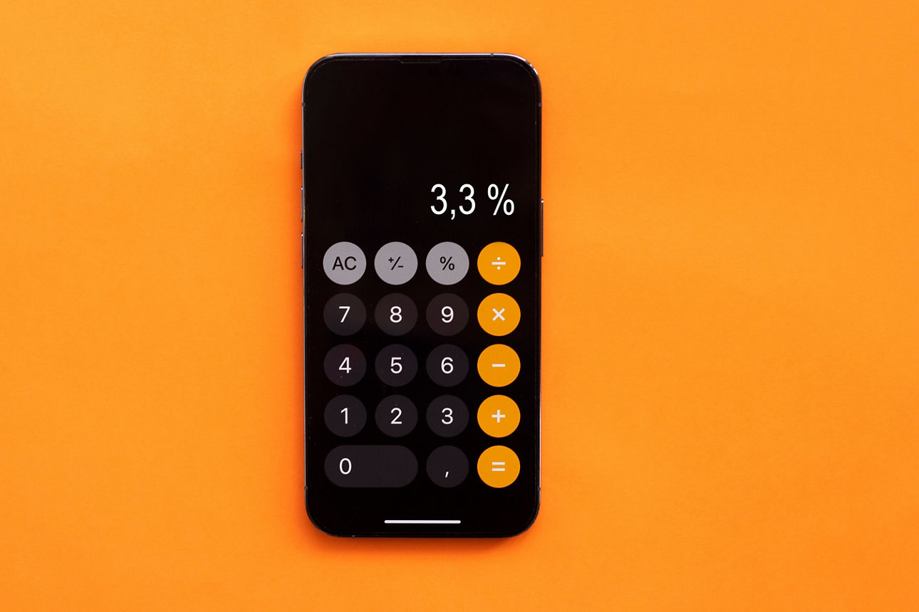 Smartphone mit geöffneter Taschenrechner-App und Anzeige von 3,3 Prozent vor orangefarbenem Hintergrund